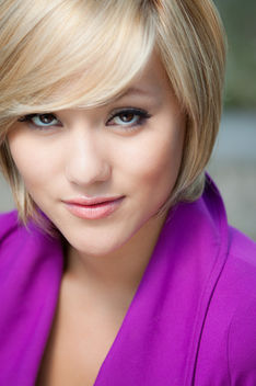 Close-up headshot of blonde woman in a vibrant purple blazer with dramatic eye makeup