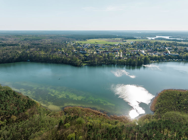 Luftaufnahme eines Sees mit angrenzender Ortschaft und Waldlandschaft in Sachsen – Symbolbild für Grundstücke mit Naturbezug und Entwicklungspotenzial.