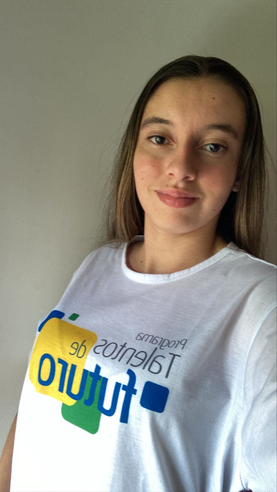 Uma jovem mulher, de cabelos longos, que veste uma camiseta branca com a logo do programa Talentos de Futuro
