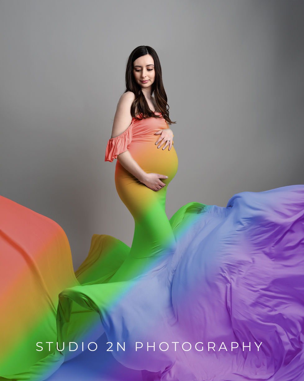 maternity photo of woman with long dark hair in a rainbow dress with skirt flourished