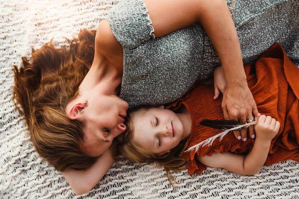 mother and daughter on knit blanket with daughter holding a feather