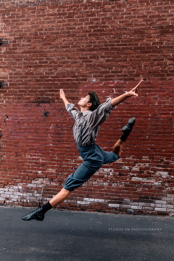 person in newsboy outfit midair in a stag leap against a brick wall