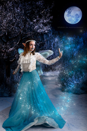 young woman in a blue dress with fair wings on a dark blue winter scene with blue sparkles swirling in front of her
