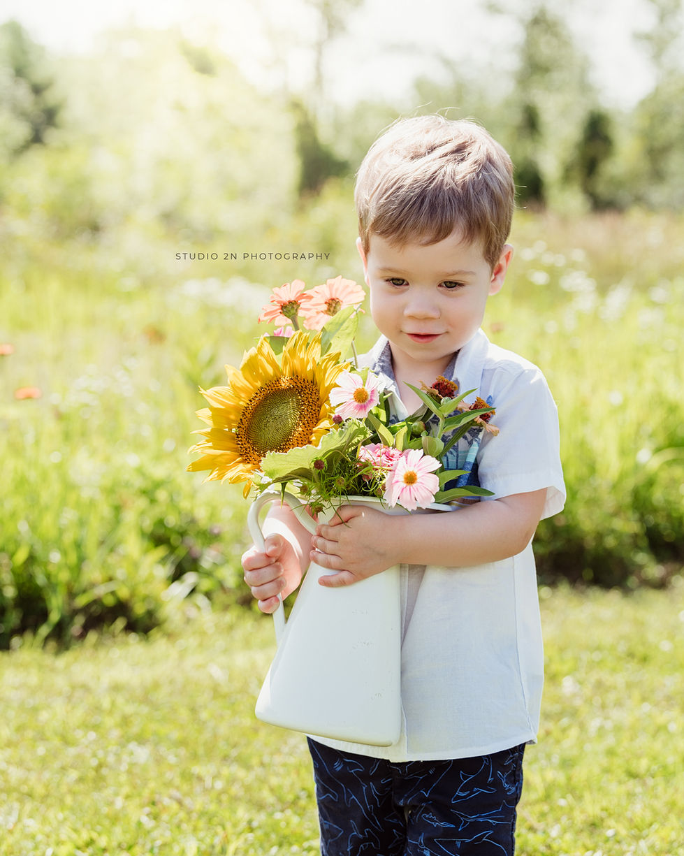 toddler boy in white shirt and shorts holding a floral bouquet in a garden
