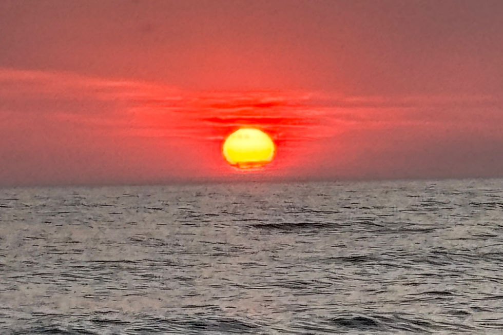 setting sun over the ocean. dark tones, the sky is a deep red and the water is calm and a dark shade of gray
