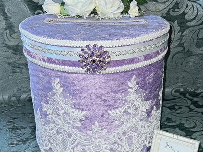 Lavender velvet box with white bridal lace and flowers, adorned with a jeweled brooch.