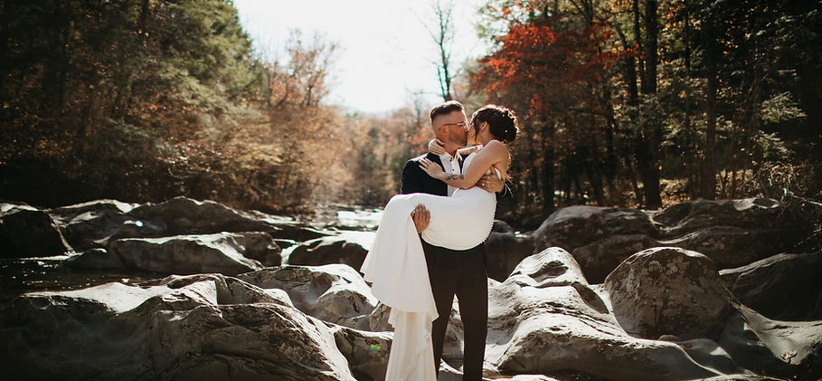 Greenbrier Gatlinburg TN Elopement with bride being carried by her groom as they kiss while walking through a dried river bed in the fall for their gatlinburg elopement 