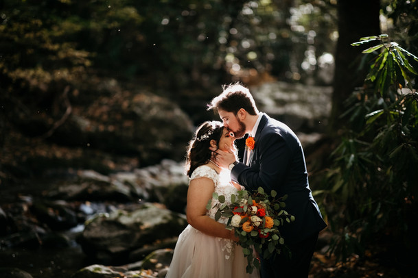 Bride in a flowing dress and groom holding hands at a forested pond at Elys Mills during a Gatlinburg elopement, photographed by Great Smoky Mountain Elopements