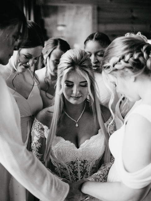 black and white wedding picture of bride surrounded by her bridesmaids as they pray together