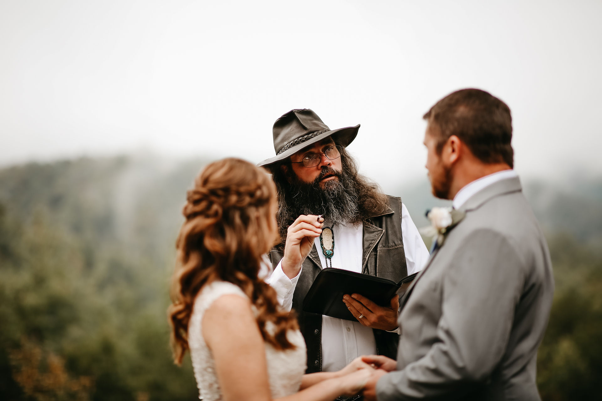 Smoky Mountain wedding ceremony in the foothills with bride and groom holding hands and looking to their Gatlinburg Wedding Officiant as he shares scriptures