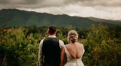 elope to gatlinburg in Cades Cove with bride and groom holding hands and looking out at the smoky mountains together in the summer with lush green trees