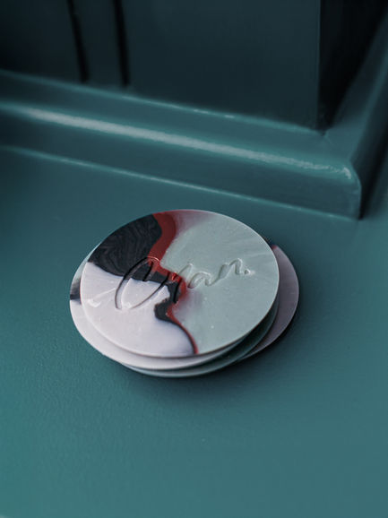 Stack of recycled plastic branded coasters with marble-effect design and bespoke debossed logo on teal surface