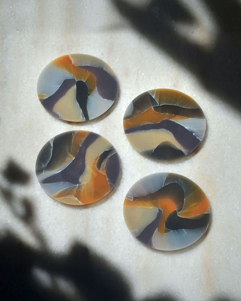 Set of recycled plastic coasters with marbled pattern in orange, lilac and cream tones on light surface