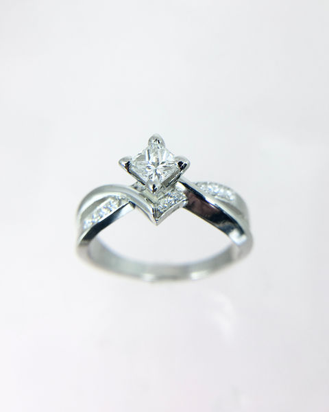 White gold ring with a princess cut diamond in a kite-shaped setting and accent diamonds along a curved band.