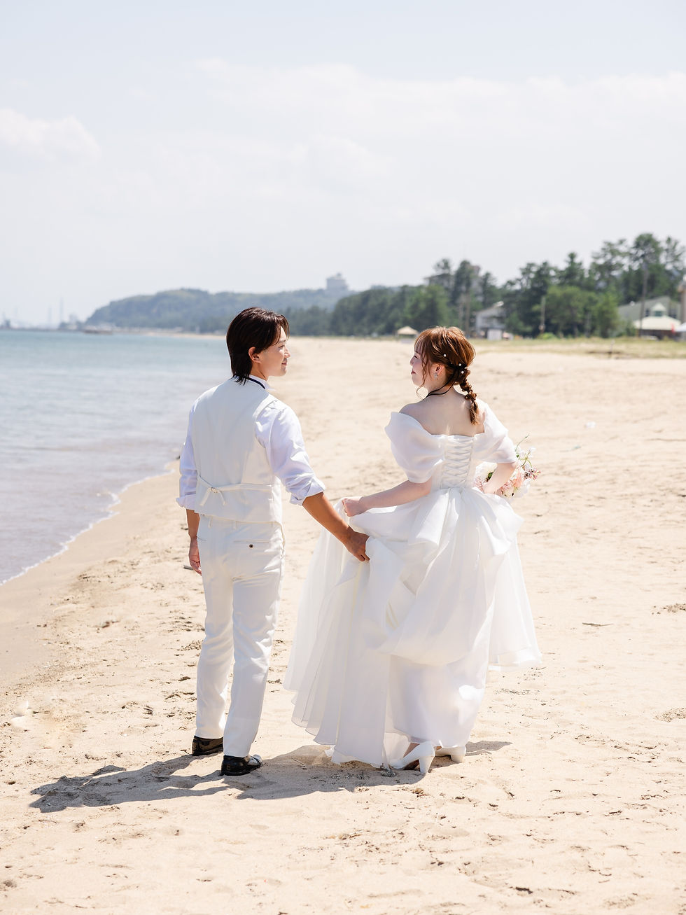 富山の海の砂浜で笑う新郎新婦