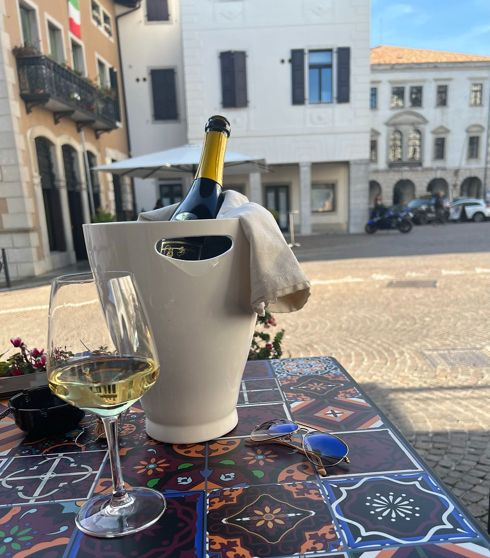 Sklenka prosecca a lahev ve chladicí nádobě na italském náměstí s barevným stolem a slunečními brýlemi