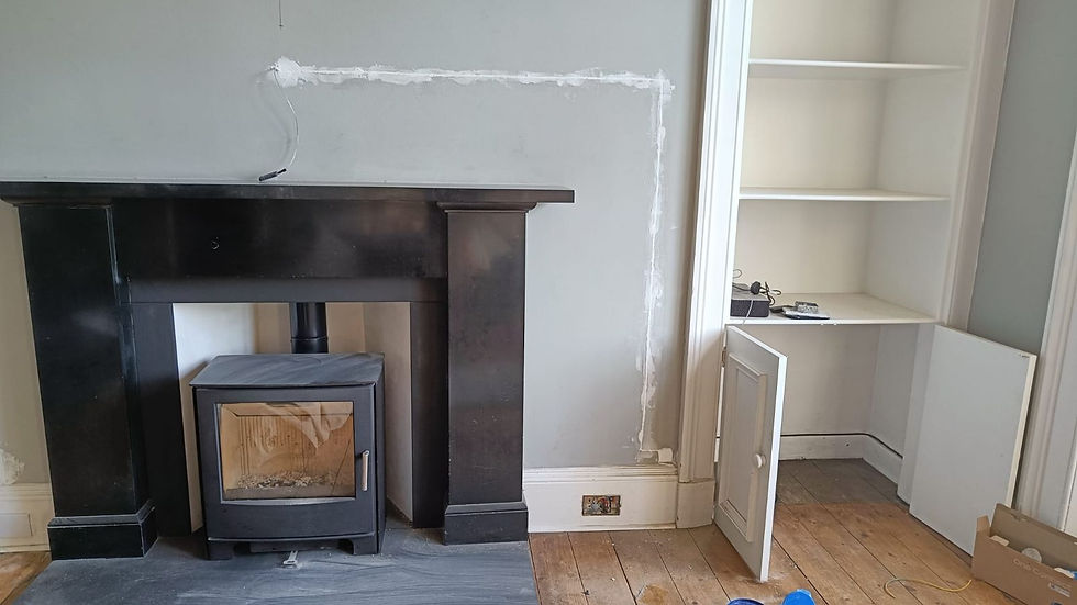 A black fireplace with cast iron fire and grey wall behind. There is a cupboard at the side. The cable raggling is on the wall in white forming a right angle from the top of the fireplace, down the wall to the cupboard.
