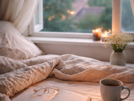 Book and pen on a bed with candle burning on windowsill