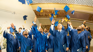 A group of graduates dressed in blue cap and gowns toss their mortar boards into the air while celebrating graduation from New Futures Career Launch professional certification program