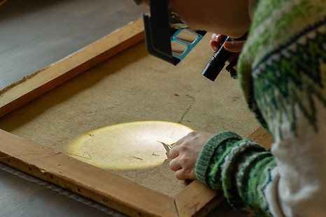 En malerikonservator undersøker et lerret med lommelykt 