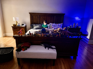 Young child sitting in bed surrounded by toy dinosaurs and stuffed animals at night, illustrating modern kids seeking comfort and connection with parents