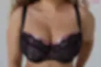 A woman posing in Ewa Michalak Rosa Bella S bra. The bra has solid black straps and pink cups, with a black lace overlay.