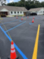 New blue ADA parking stall lines and yellow striping with traffic cones blocking off wet paint at an office parking lot in Pensacola, FL