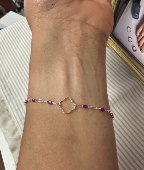 A silver permanent bracelet with red beads and a clover connector.