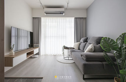 在信義區這處充滿日光的寓所中，設計的核心在於「邊界的消融」，大膽採用黑框玻璃滑門界定餐廚空間，不僅優化了室內的通透感，更讓自然光能無礙地穿透至每一個角落，建構出寬闊且層次分明的開放式格局。

空間以極簡的純白與暖木為基調，玄關處巧妙運用灰色幾何六角磚與室內地坪進行非對稱銜接，以材質的自然轉換定義落塵區的序幕。公領域中，具有歐美輪廓的藤編沙發與木質家具，在線性照明的洗禮下，展現出一種隨性且優雅的生活姿態。

私領域則轉向柔和的色調敘事，分別運用低飽和的莫蘭迪綠與粉色調勾勒出臥室的靜謐氛圍，讓每一次休息都如同置身於自然律動之中。沐曦以細膩的工程筆觸，將收納機能與建築線條完美整合，讓家不再只是居住的場所，而是一處可以自由呼吸、承載溫度、充滿藝術張力的「生活的容器」。