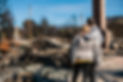 couple standing in front of and looking at the rubble of a burned down home