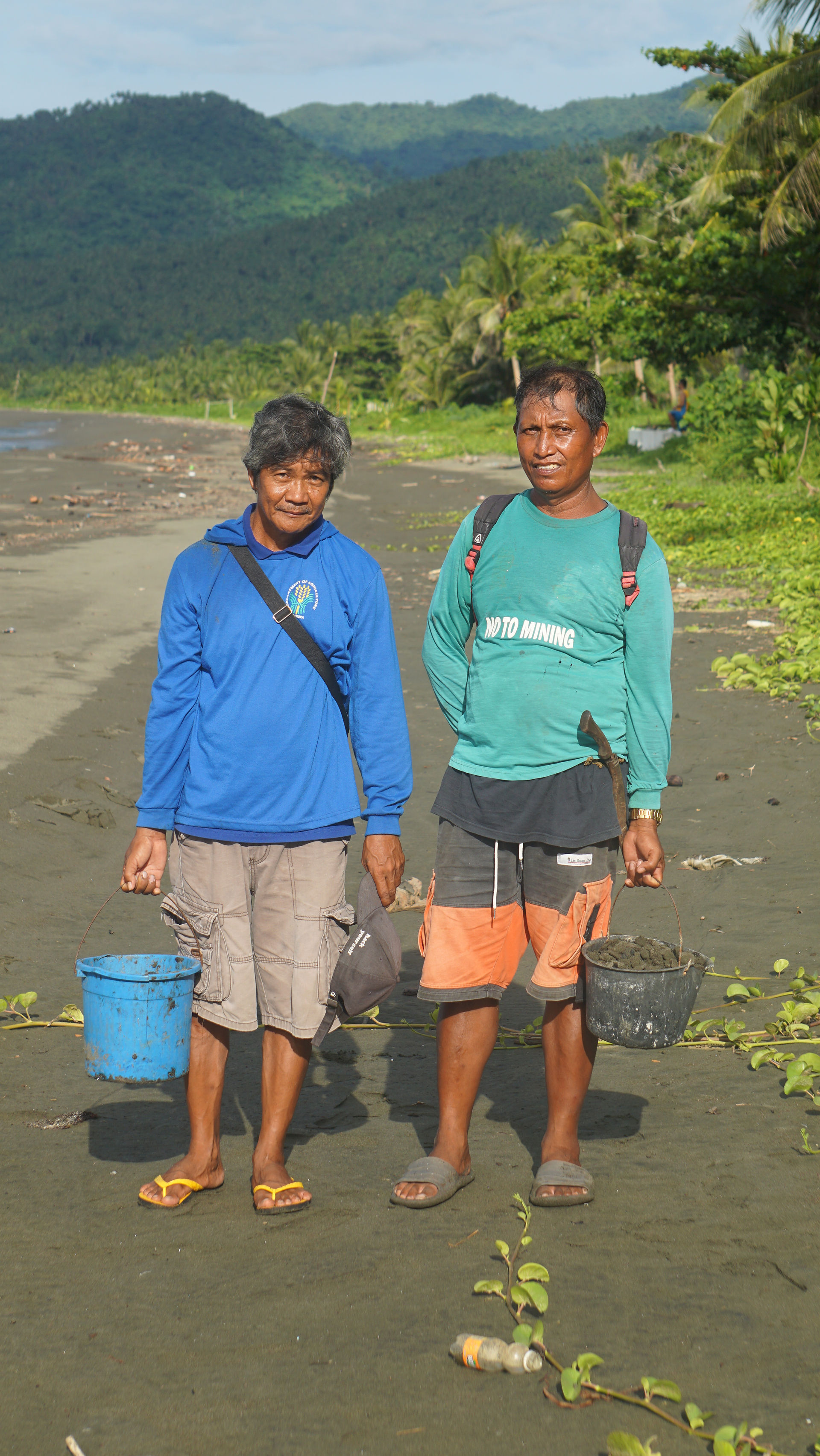 Fisherfolks in Kabilang Ibayo beach holding buckets of tar balls covered in sand.