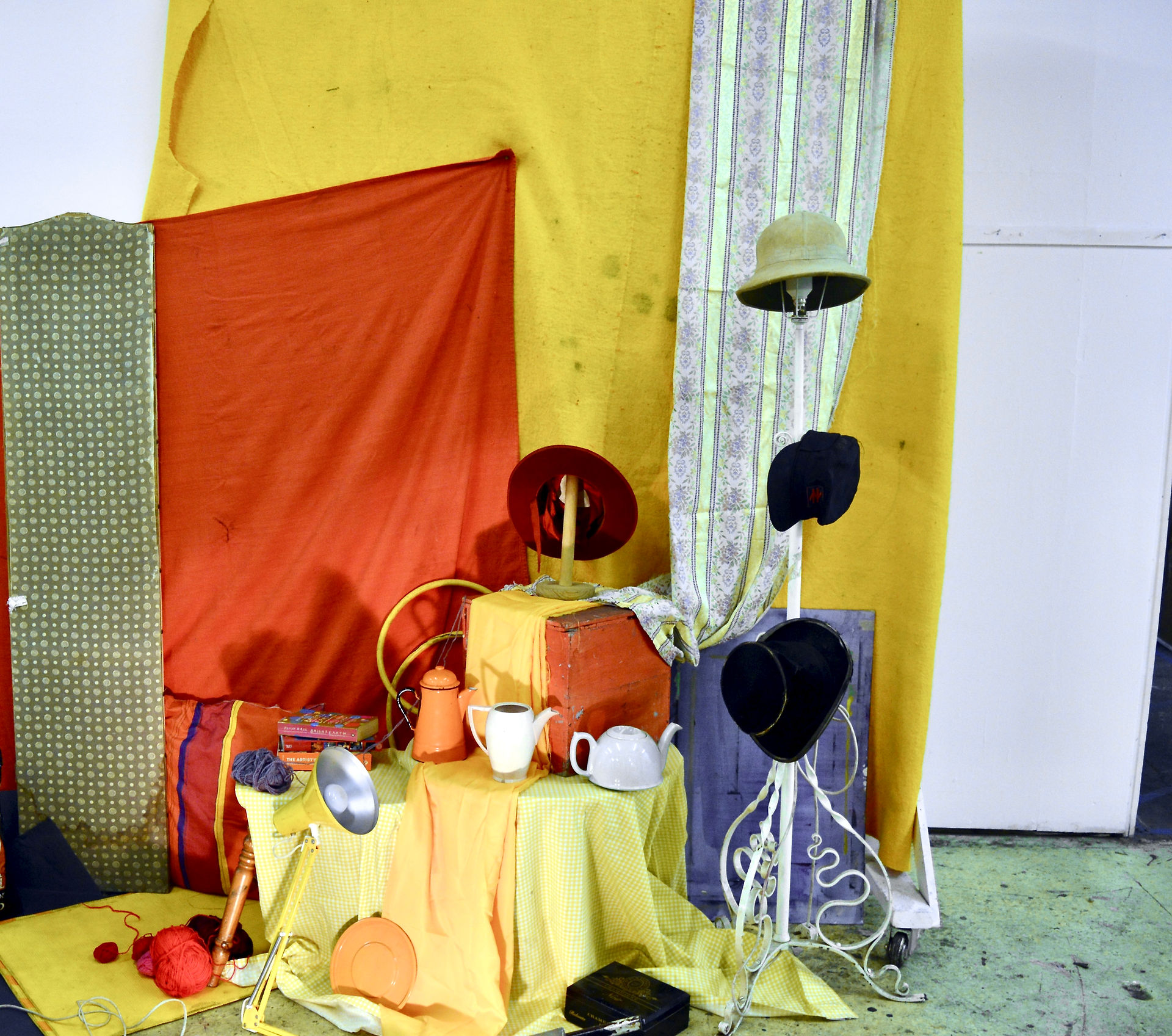 Red and yellow setup with hats, teapots, and patterned clothsPlayful groupings of everyday objects with bold, contrasting colours.
