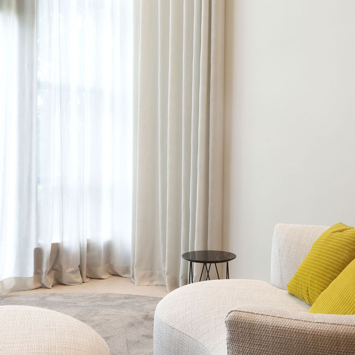 Sofa und Hocker mit Blick auf eine Fensterwand mit Gardinen