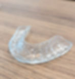 A clear custom night guard placed on a wooden surface, showing protective appliance for teeth grinding in Singapore.