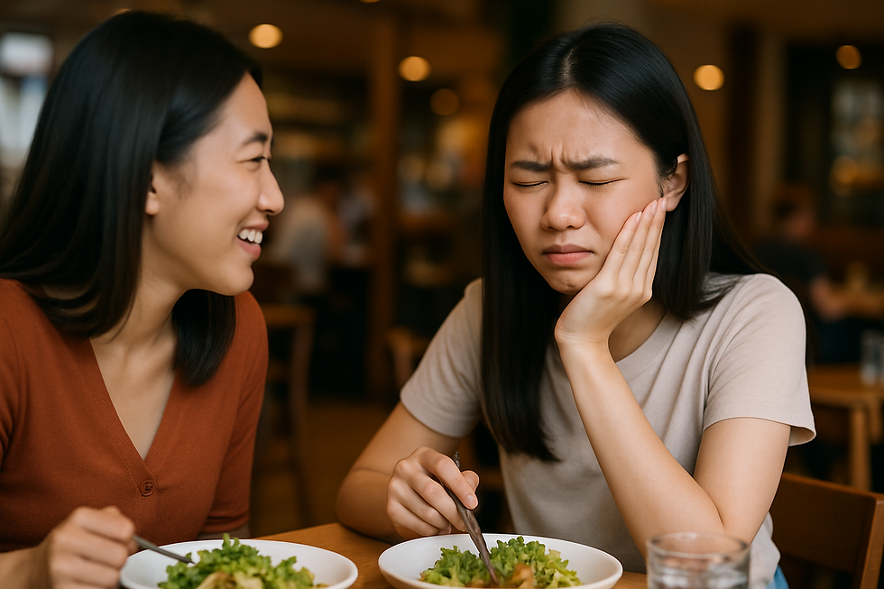 Young Asian woman holding her cheek in discomfort while chewing at a restaurant, showing possible tooth pain when biting, with a concerned friend beside her.