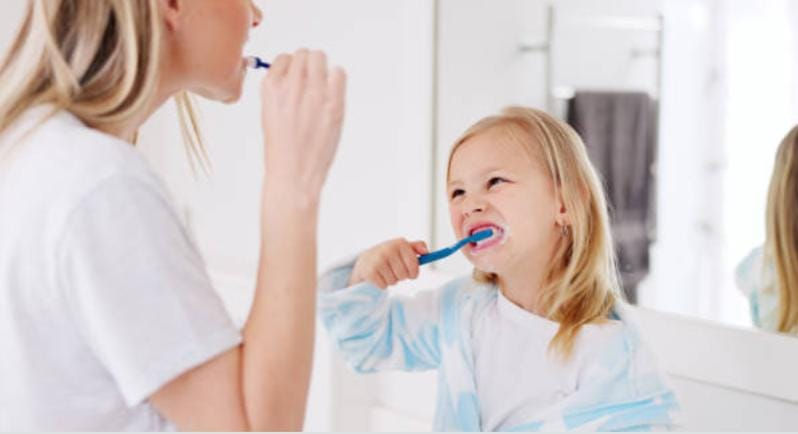 Mother and daughter brushing their teeth together, demonstrating daily oral care to maintain tooth crowning