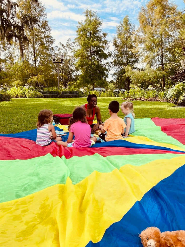 Yolonda Deon Tyler, Mindful Play Learning Certified Facilitator, playing with children on a rainbow tarp