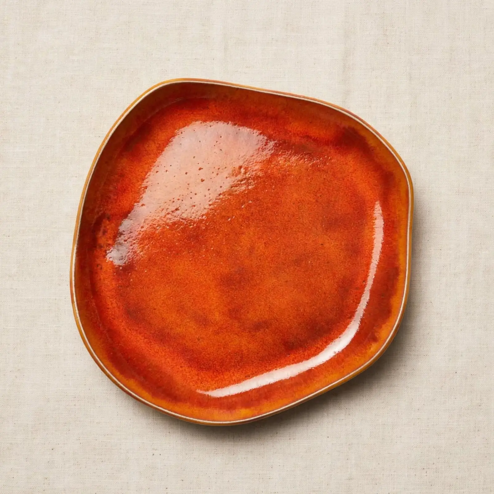 Assiette organique en grès faite main avec émail brillant orange brûlé et caramel sur fond en lin naturel.