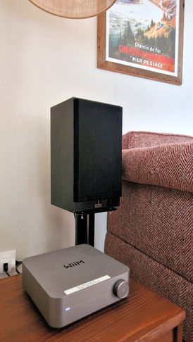 Gros plan sur le système audio Wiim et une enceinte noire dans le salon du studio Les Cristaux à Combloux, avec affiche vintage de montagne au mur.