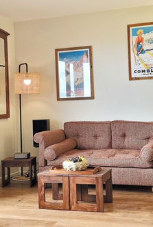 Espace salon du studio Les Cristaux à Combloux avec canapé vintage en tissu brun, table basse en bois et affiches de montagne encadrées au mur.