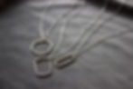 Silver geometric necklaces on a soft gray velvet background.