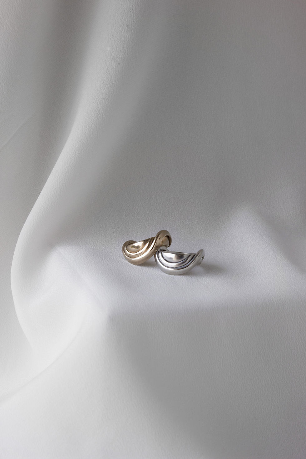 Thumbnail: front view of two rings sitting on top of each-other. Background is draped white satin with soft shadows. 