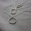 Thumbnail: Various silver geometric necklaces on a soft white fabric background with very dark and muted light.