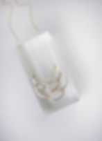 Gold necklace on a clear, resin rectangle prop on an off-white background