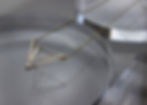 Close up of Gold Fill geometric layered Acute Triangle necklace, featuring two overlapping triangles, one wider than the other. Prop is a clear round resin. Light is dark. 