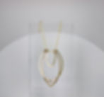 Gold Fill Small Flame Necklace. A design of three tiers of upside down tear drop shapes varying from long to wide to small and center. Design is an abstract version of a flame. This is the small version of the design. 
Prop is a clear resin rectangle lighting is  bright and white. A white half circle is featured behind the clear resin prop. 