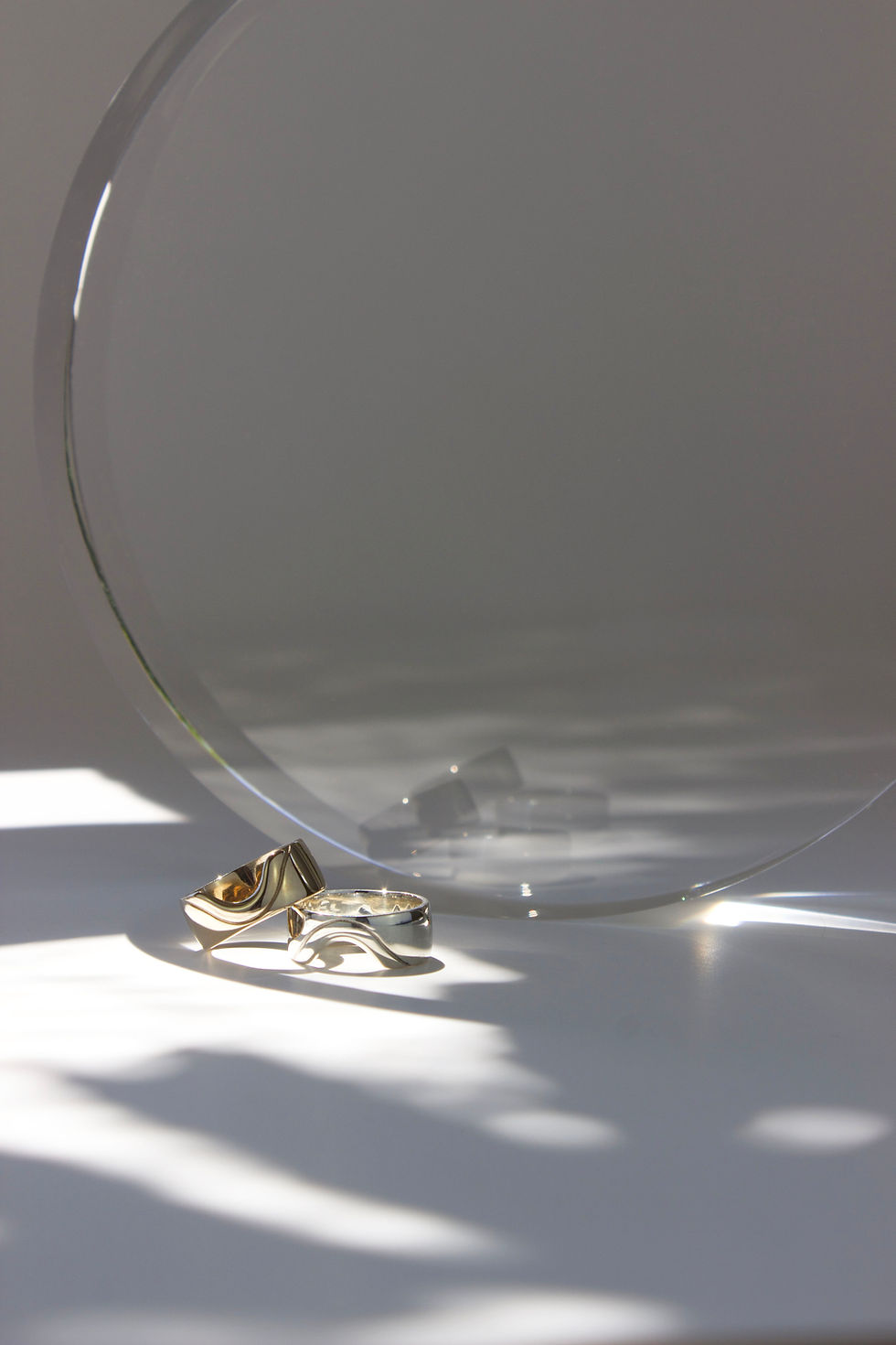 Thumbnail: Silver and gold tone ring on white background with large clear round resin prop in the background. Dappled light and shadows in the foreground. 