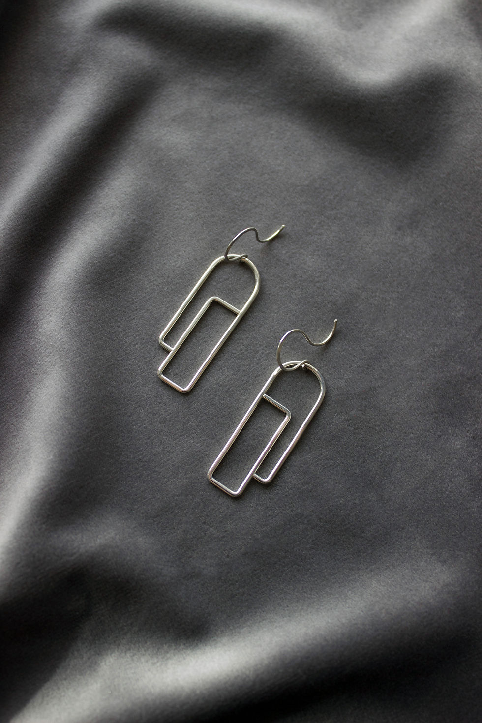 Thumbnail: Geometric silver wire "profile" earrings on a dark grey velvet background with clear resin props. 