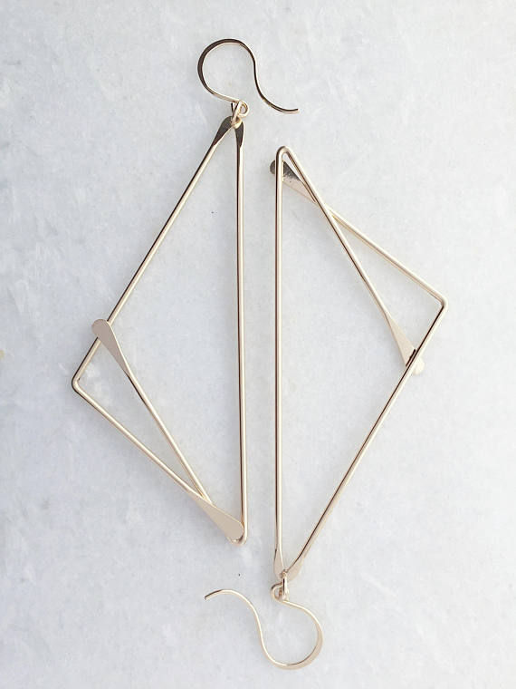 Thumbnail: Gold Fill view of fox earrings on white marble. Earrings are large art deco style, each earring featuring half triangles with one smaller triangle on each side, when put together, resembles an abstract version of the shape of a fox face. 