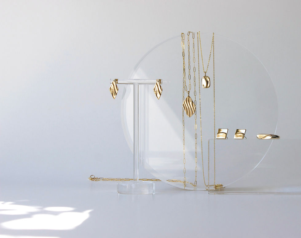 Thumbnail: Various gold tone, jewelry on clear, resin props with dappled light and off-white background.